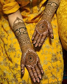 a woman's hands with hennap on her hand and yellow dress in the background