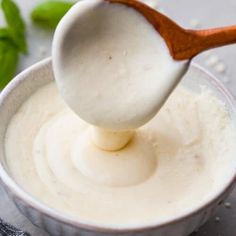 a wooden spoon scooping some white sauce out of a small bowl with basil on the side