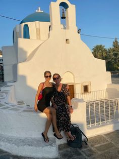 two women sitting on steps in front of a white building with a bell tower and blue dome