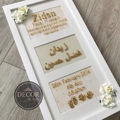 a white frame with some gold lettering and flowers on the floor in front of it