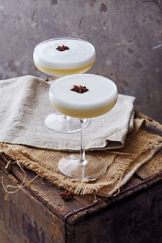 two glasses filled with drinks sitting on top of a wooden table next to a cloth