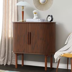 a wooden cabinet sitting next to a chair in front of a wall with a clock on it