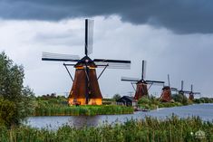 several windmills are standing near the water under a cloudy sky