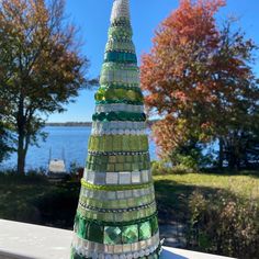 a bottle cap christmas tree sitting on top of a white fence next to trees and water