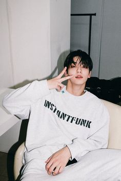 a young man sitting in a chair with his hand up to his face while wearing a white sweatshirt