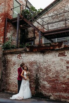 a bride and groom standing in front of an old brick building