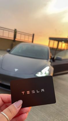 a person holding up a black business card in front of a car on the road