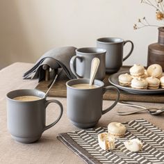 two cups of coffee sit on a table next to plates with pastries and spoons