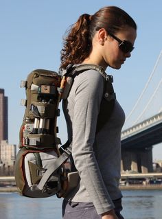 a woman with a backpack on her back walking by the water in front of a bridge