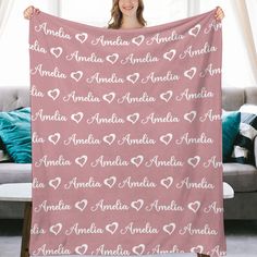 a woman holding up a pink blanket with hearts on it in front of a couch