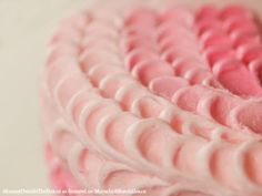 a close up view of a pink cake with white frosting in the form of waves