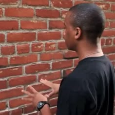 a man standing in front of a brick wall with his hands out to the side