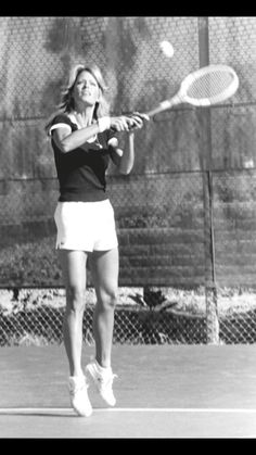 a woman swinging a tennis racquet on top of a tennis court in front of a fence