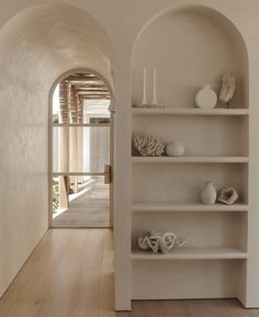 an arched doorway leads into a white room with shelves and vases on the wall