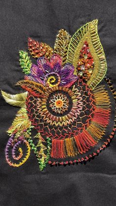 an embroidered piece with colorful flowers and leaves on it's side, sitting on a black background