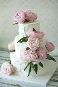 a three tiered white cake with pink peonies on the top and bottom