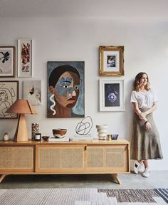 a woman standing in front of a wall with pictures on it and paintings above her