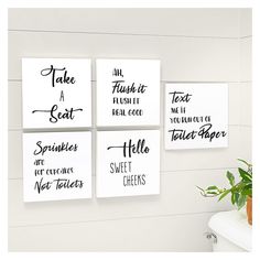 four white canvases with black lettering on the wall above a potted green plant