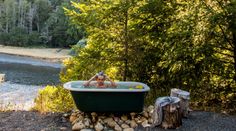 a woman taking a bath in a green tub surrounded by rocks and trees next to a river