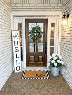 a welcome mat on the front door of a house with white flowers and a wreath