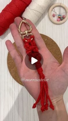 a hand holding a red rope with a gold hook on it and yarn spools in the background