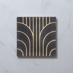 a square black and gold tile with lines on the bottom, against a white wall