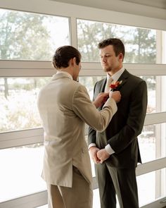 two men standing next to each other in front of a window wearing suits and ties