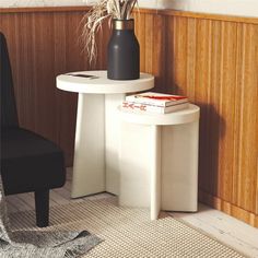 a white table with a black vase sitting on top of it next to a chair