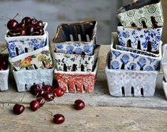 four ceramic bowls with cherries in them on a wooden table next to two cherries