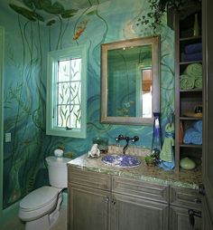 a bathroom decorated in green and blue with fish painted on the walls, along with a toilet