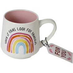 a white coffee mug with a rainbow painted on the side and a tag attached to it