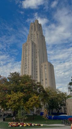 a very tall building sitting next to a lush green park under a blue cloudy sky