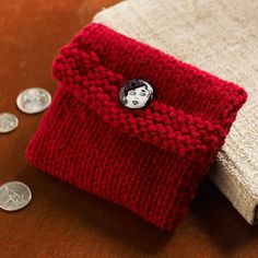 a red and white knitted bag sitting on top of a table next to some coins