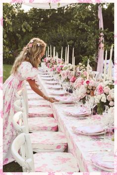 a woman in a pink dress is setting a table with white and pink flowers on it