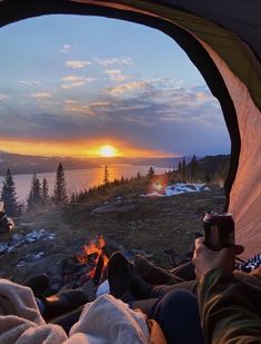 a person sitting in a tent next to a fire with the sun setting behind them