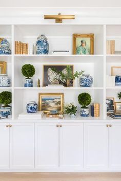 a white bookcase with blue and white vases on it's shelves next to books