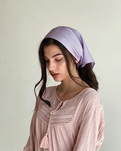 a young woman wearing a pink blouse and a purple head scarf is standing in front of a white wall