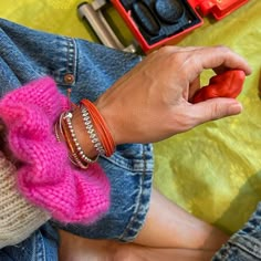 a woman wearing pink and red knitted bracelets next to an orange toy truck