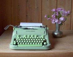 a green typewriter sitting on top of a wooden table next to a vase with flowers