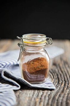 a glass jar filled with spices sitting on top of a wooden table next to a blue and white towel