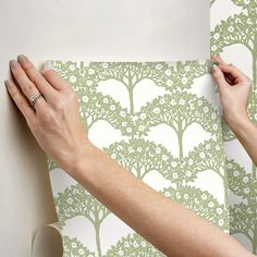 a woman is painting a wall with green and white tree stencils on it