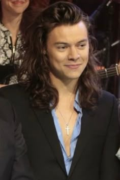 a man with long hair wearing a black suit and blue shirt smiling at the camera