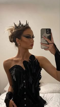 a woman taking a selfie with her cell phone wearing a black dress and tiara