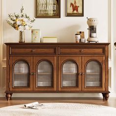 a wooden cabinet with glass doors in front of a white rug and two pictures on the wall