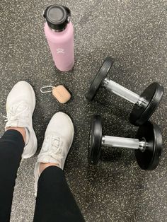 a person standing next to two dumbbells and a pink water bottle on the ground