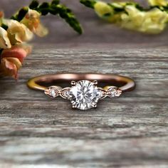 an engagement ring with three diamonds on it and some flowers in the background, sitting on a wooden surface