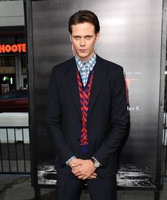 a man wearing a suit and tie standing in front of a poster