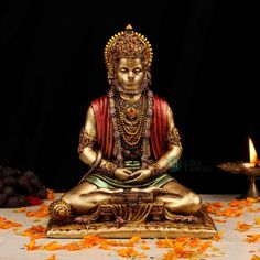 a golden buddha statue sitting on top of a table next to a lit candle and orange petals