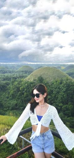 a woman standing on top of a metal rail next to lush green hillside covered in clouds