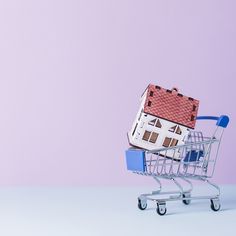 a miniature house sitting on top of a shopping cart in front of a purple wall